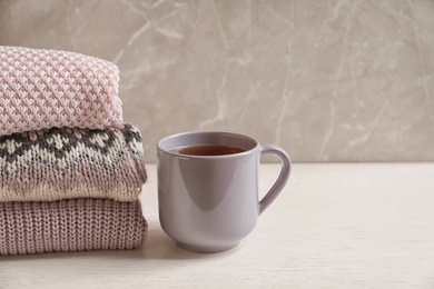 Photo of Stack of warm knitted clothes and cup of tea on table