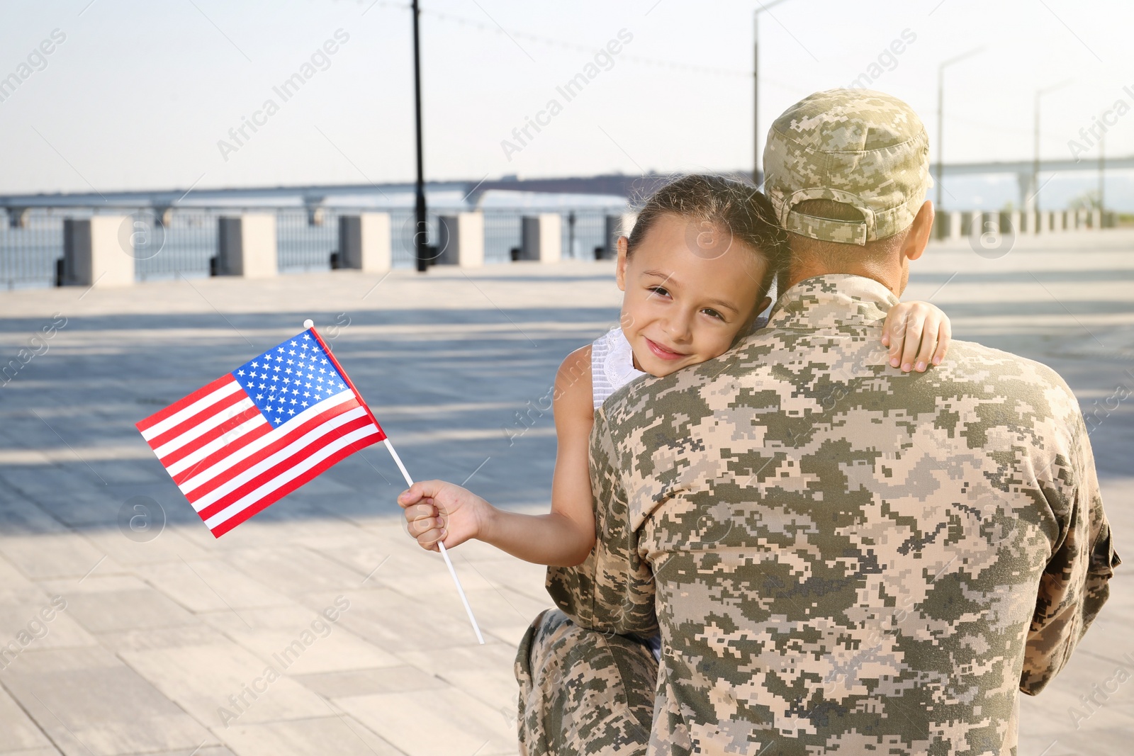 Photo of Soldier and his little daughter with flag of USA hugging outdoors