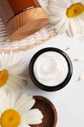 Flat lay composition with jar of face cream and beautiful flowers on white background