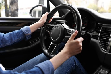 Woman holding steering wheel while driving her car, closeup