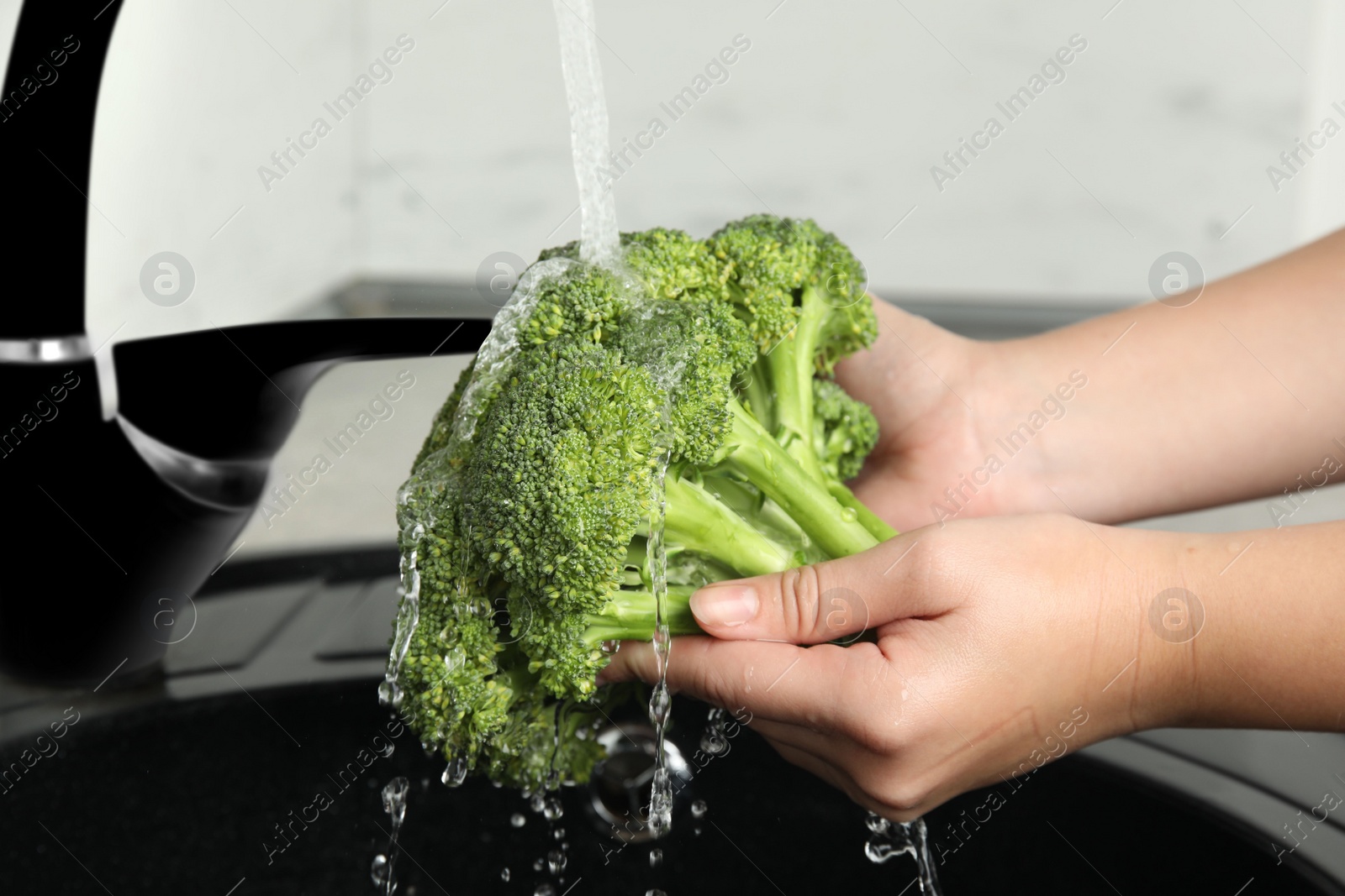 Photo of Woman washing fresh green broccoli in kitchen sink, closeup