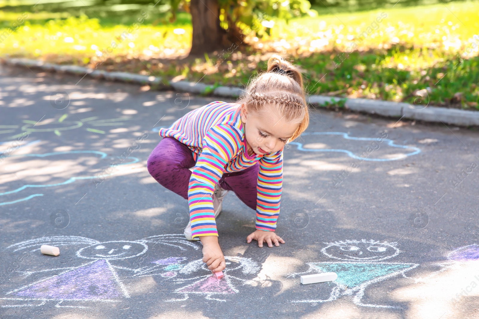 Photo of Little child drawing with colorful chalk on asphalt