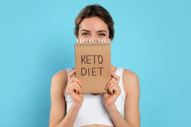 Photo of Woman holding notebook with phrase Keto Diet on light blue background