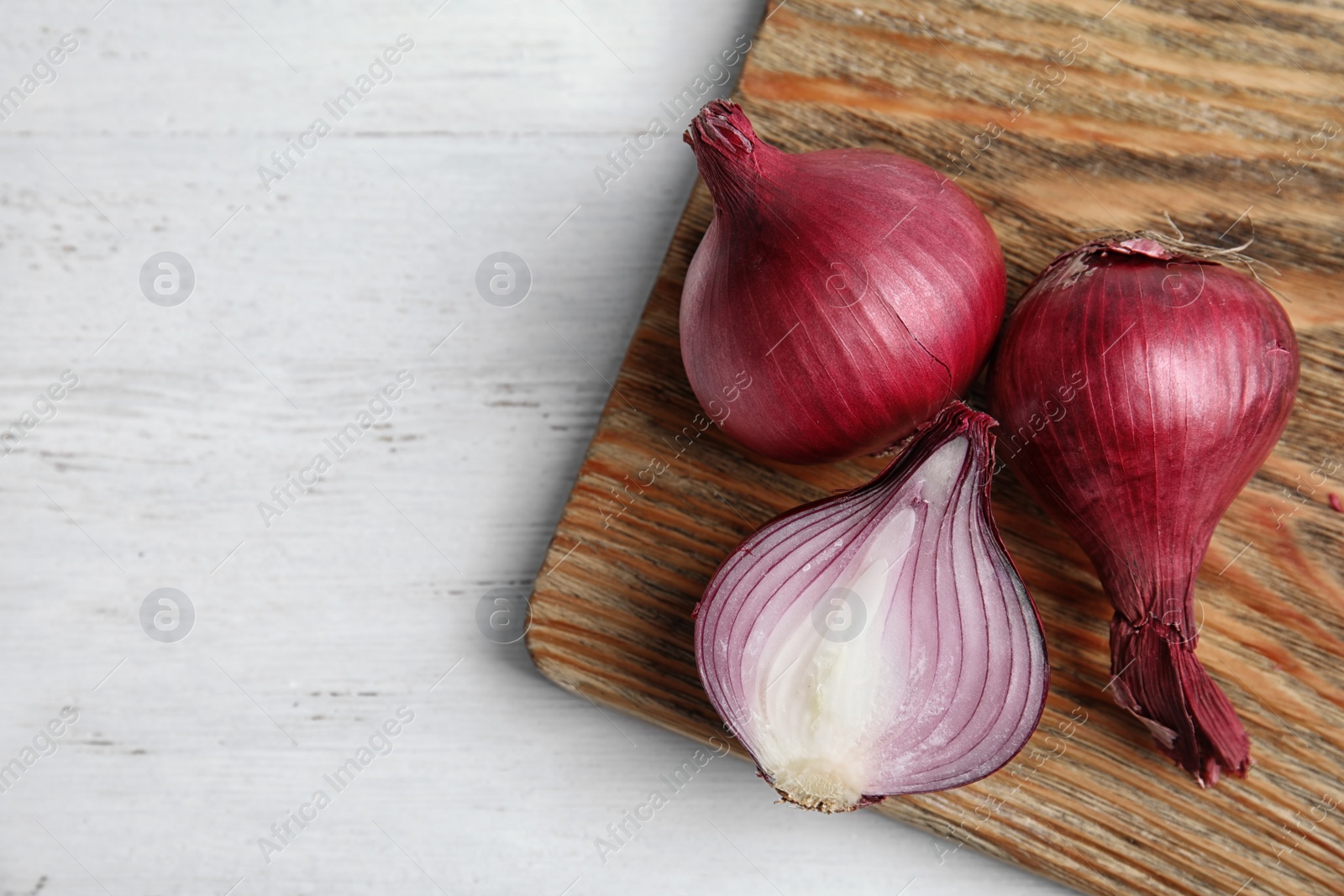 Photo of Wooden board with ripe red onions on table, top view