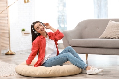 Photo of Young woman with headphones enjoying music on floor in living room