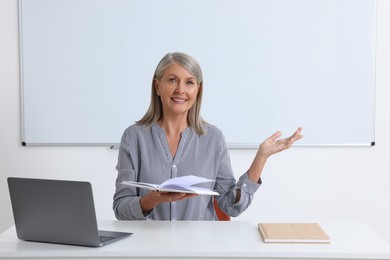 Photo of Happy professor giving lecture near laptop at desk in classroom