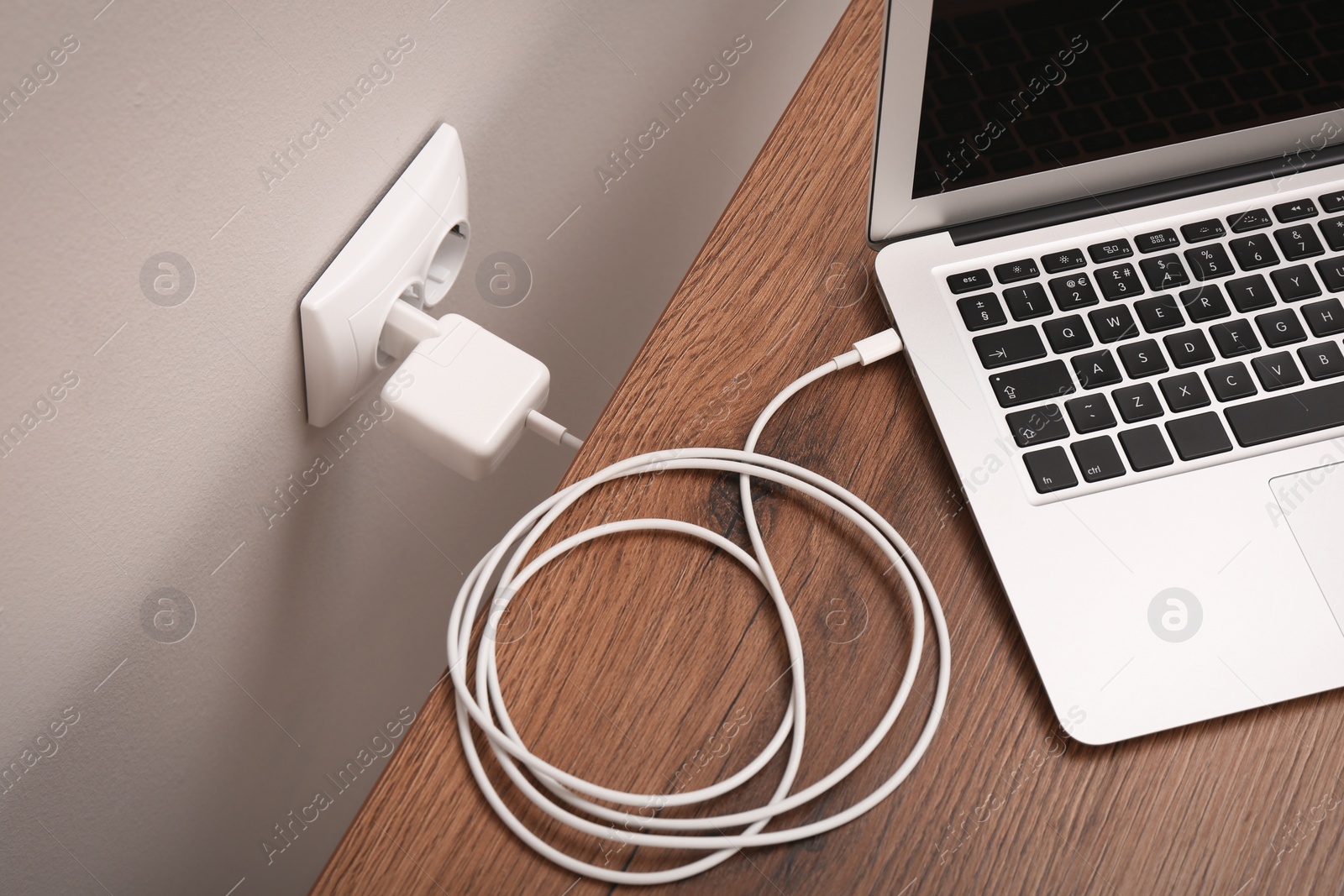 Photo of Charging laptop with power adapter in electrical socket on wooden table