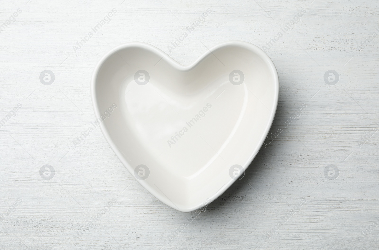 Photo of Heart shaped plate on white wooden background, top view