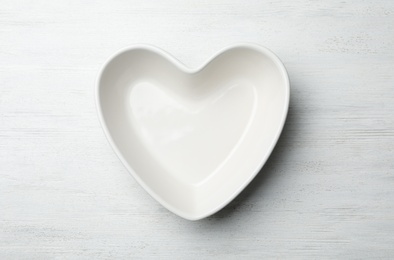 Heart shaped plate on white wooden background, top view