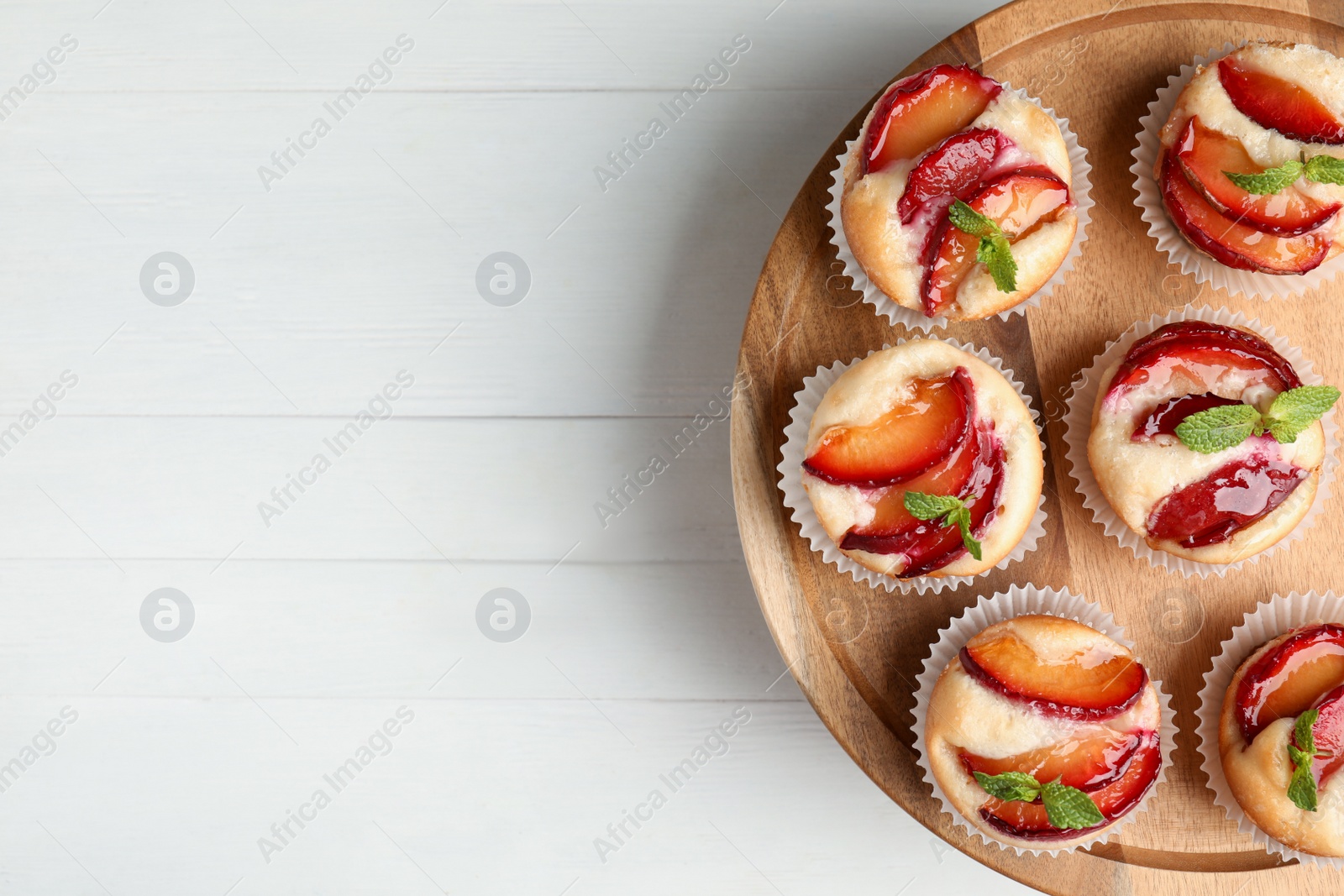 Photo of Delicious cupcakes with plums on white wooden table, top view. Space for text