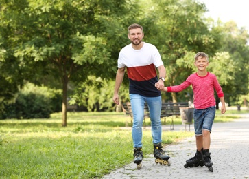 Father and son roller skating in summer park