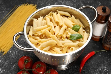Cooked pasta in metal colander, products and spices on dark textured table, closeup