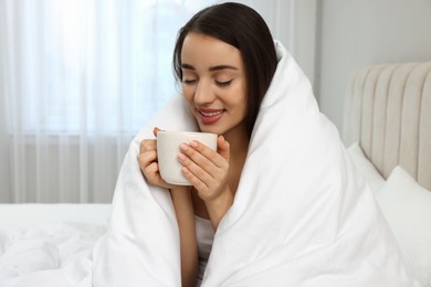 Photo of Beautiful young woman with cup of drink wrapped in blanket at home