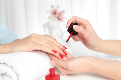 Photo of Manicurist painting client's nails with bright polish in salon, closeup