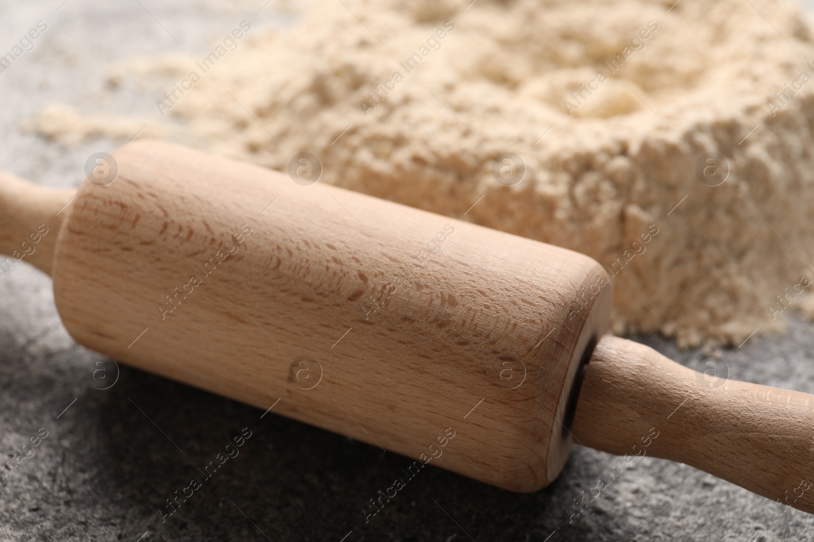 Photo of Rolling pin and scattered flour on grey textured table, closeup