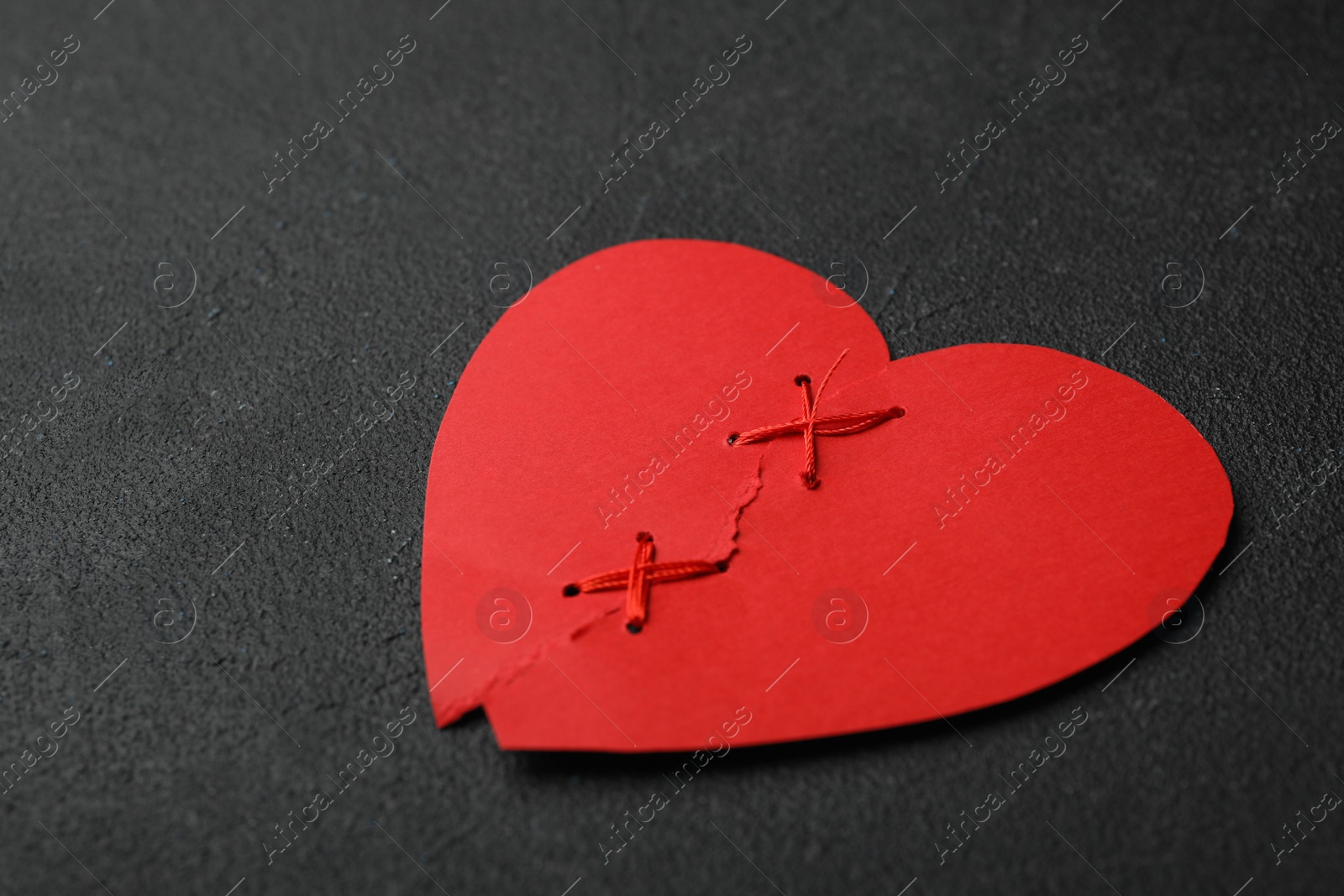 Photo of Torn paper heart sewed with thread on black stone background. Relationship problems concept