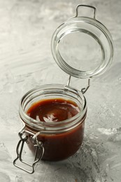 Photo of Tasty barbeque sauce in open jar on grey textured table, closeup