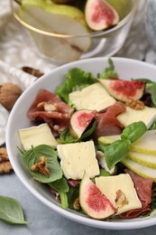 Photo of Tasty salad with brie cheese, prosciutto, pear and figs on grey table