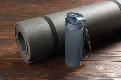 Yoga mat and bottle of water on wooden floor