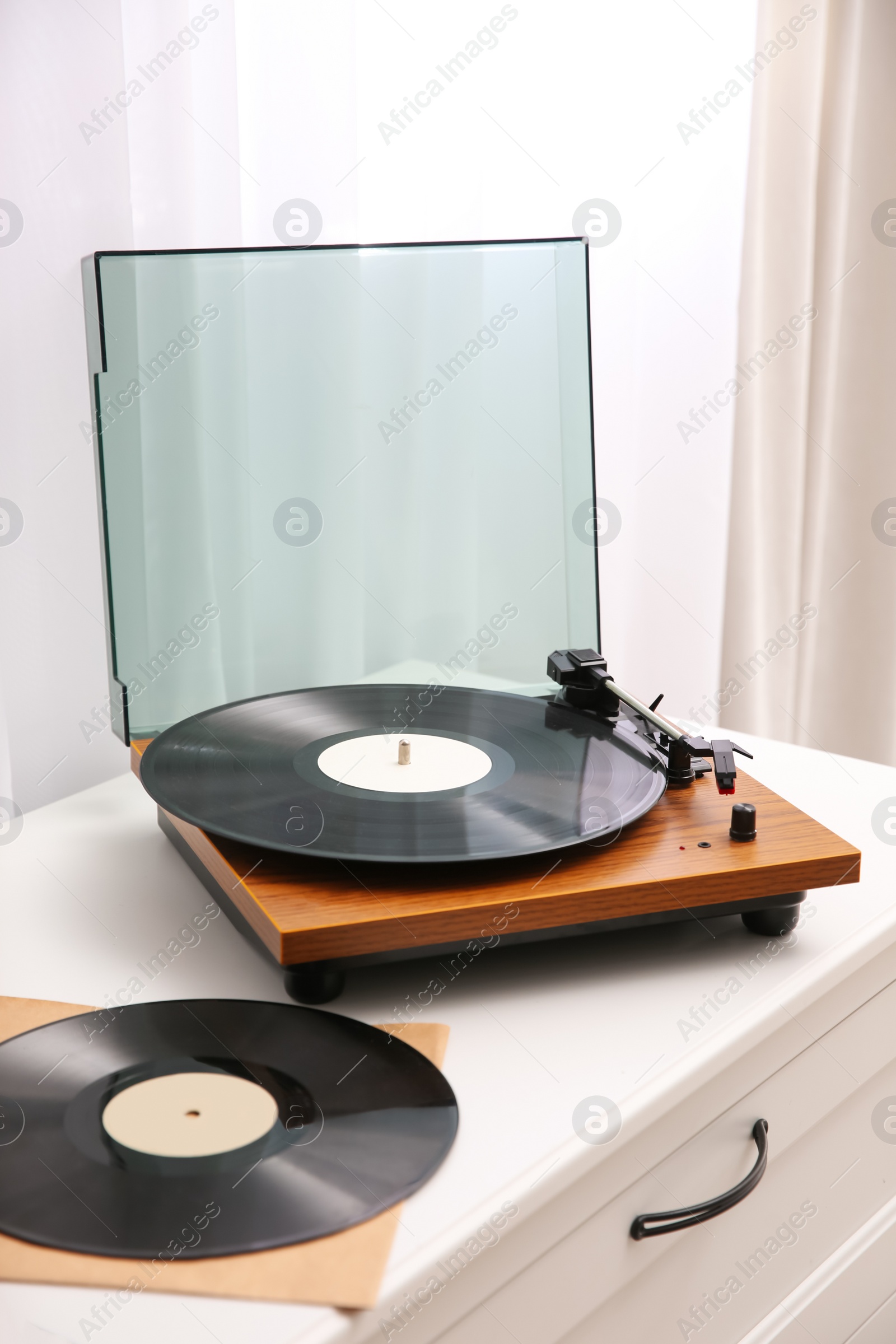 Photo of Stylish turntable and vinyl records on white chest of drawers indoors