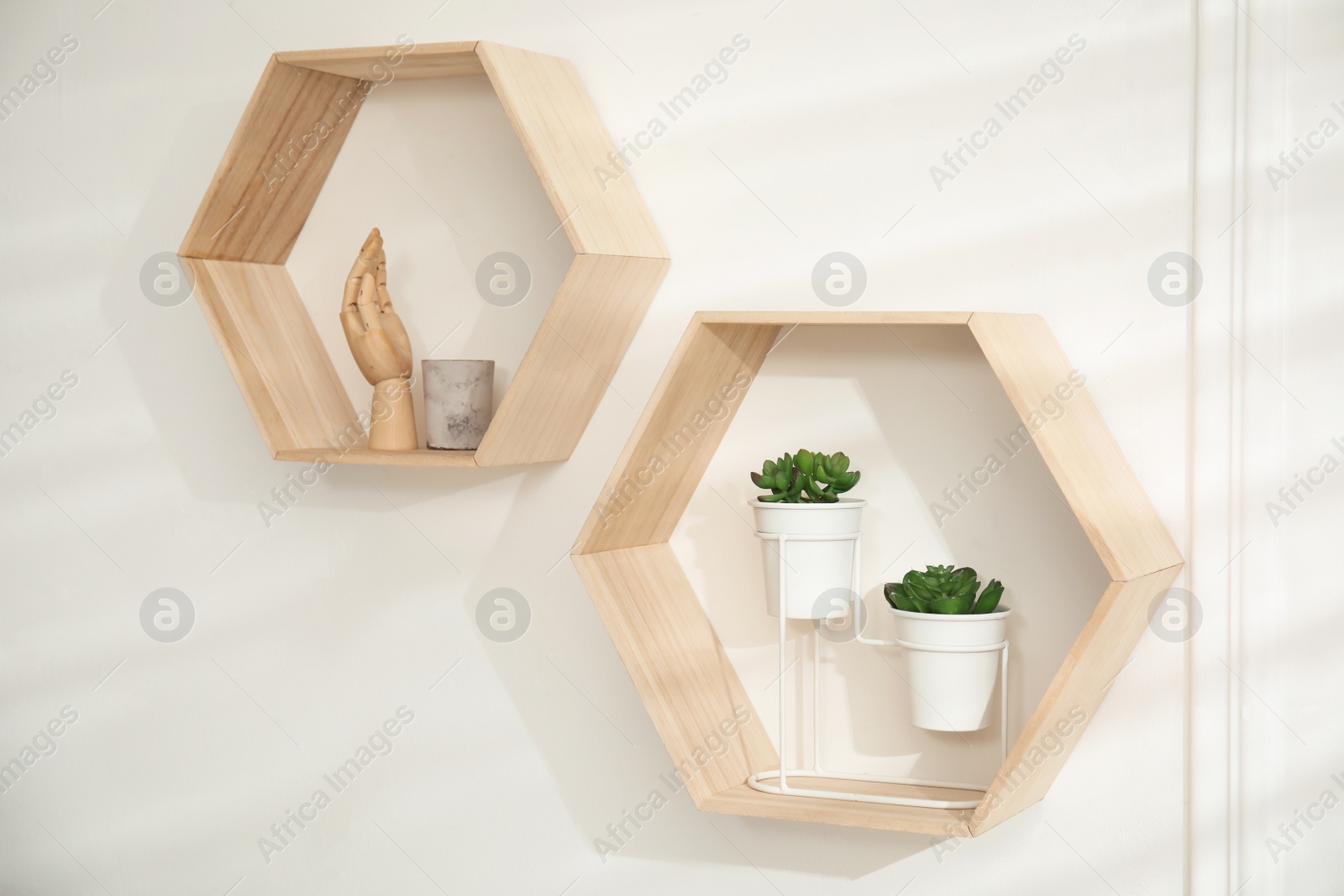 Photo of Honeycomb shaped shelves with decorative elements and houseplants on white wall