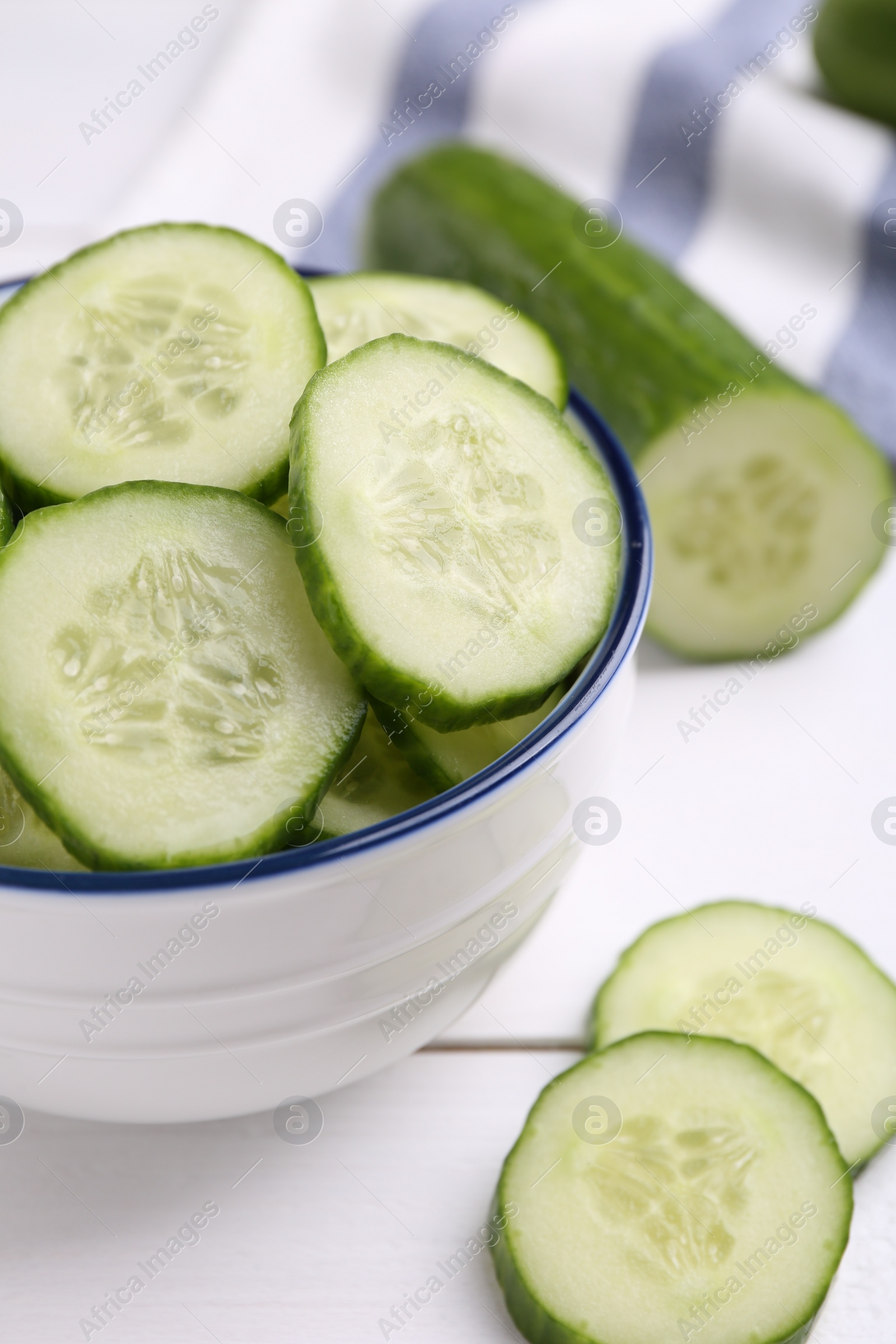 Photo of Cut cucumber in bowl and fresh vegetable on white wooden table, closeup