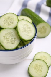 Photo of Cut cucumber in bowl and fresh vegetable on white wooden table, closeup