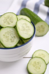 Cut cucumber in bowl and fresh vegetable on white wooden table, closeup