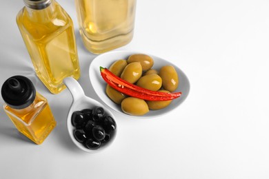 Bottles of different cooking oils and olives on white background, above view