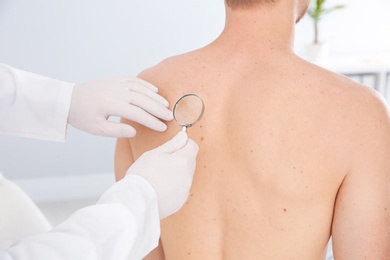 Photo of Dermatologist examining patient's birthmark with magnifying glass in clinic, closeup