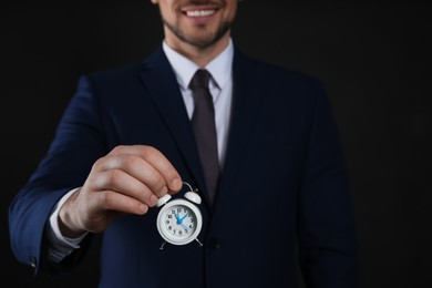 Happy businessman holding tiny alarm clock on black background, closeup. Time management