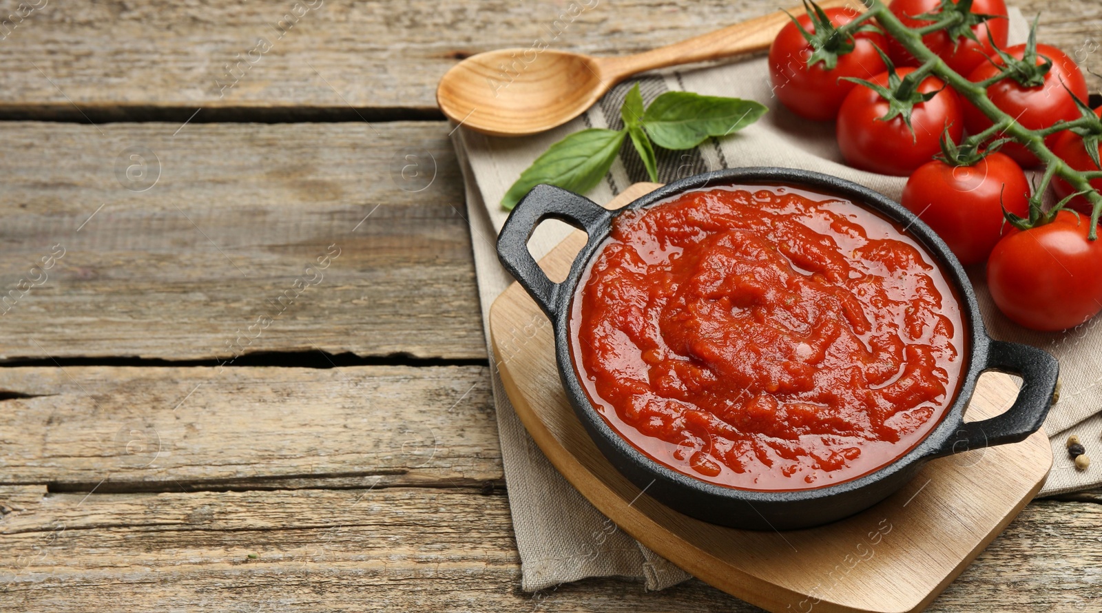 Photo of Homemade tomato sauce in bowl, spoon and ingredients on wooden table, space for text