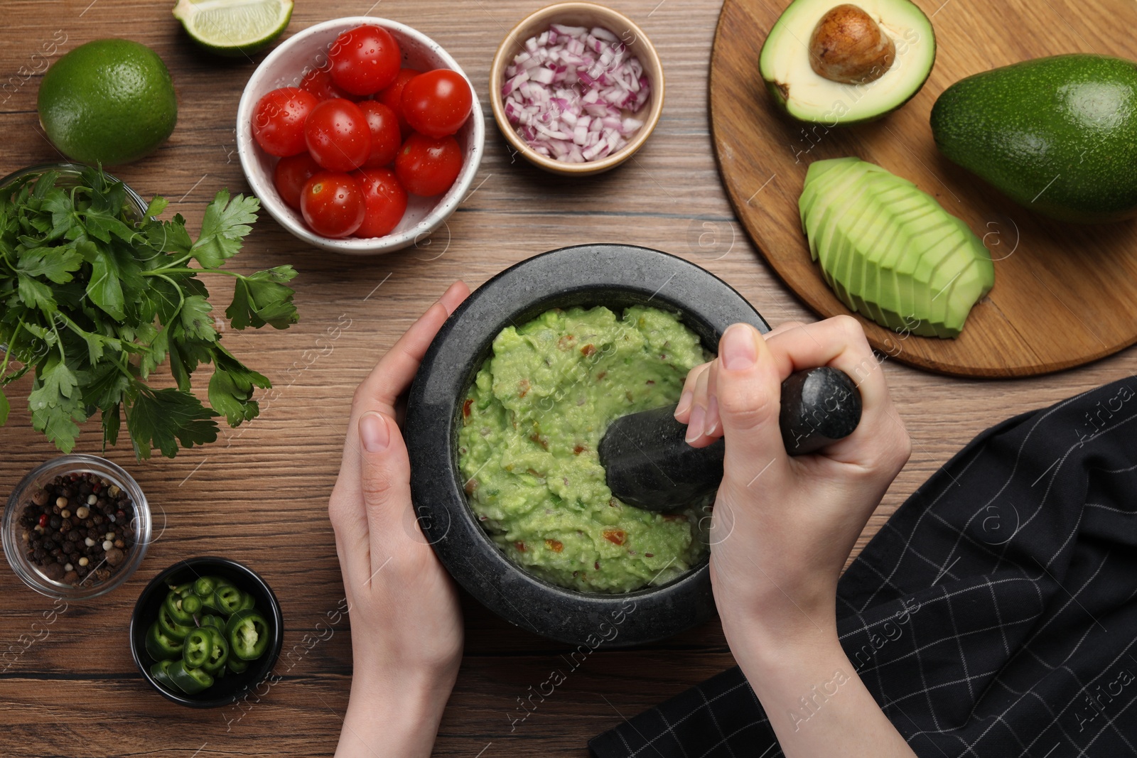 Photo of Woman preparing delicious guacamole at wooden table, top view