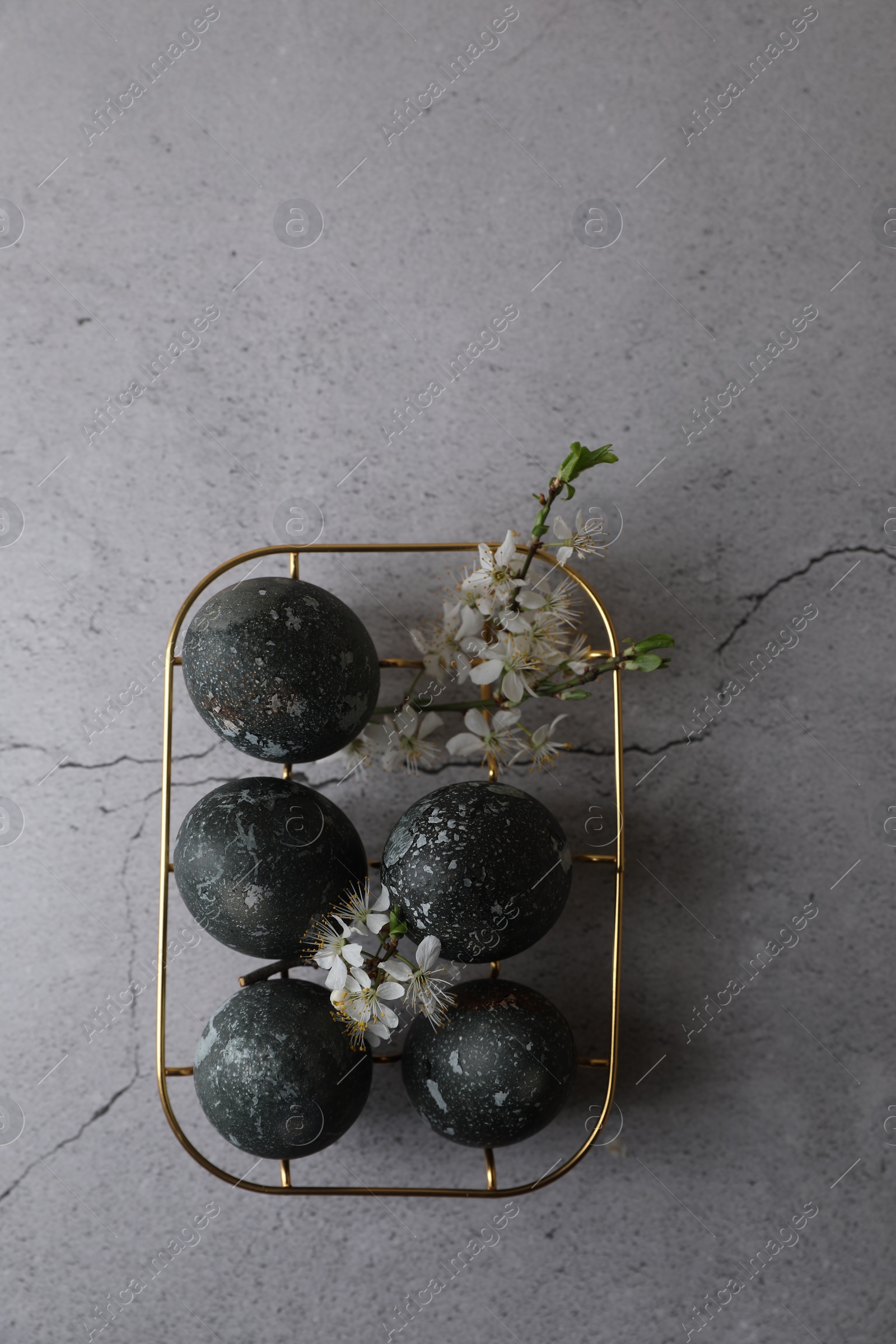 Photo of Decorated Easter eggs and flowers on grey table, top view