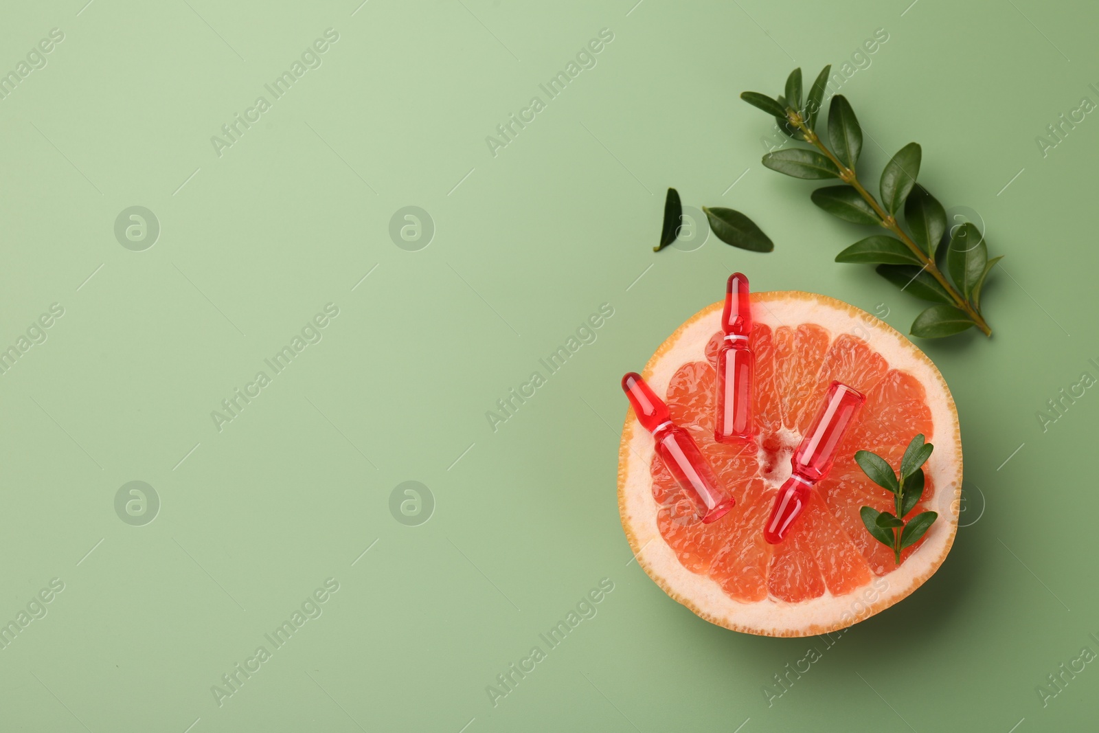 Photo of Skincare ampoules with vitamin C, half of grapefruit and leaves on light green background, flat lay. Space for text