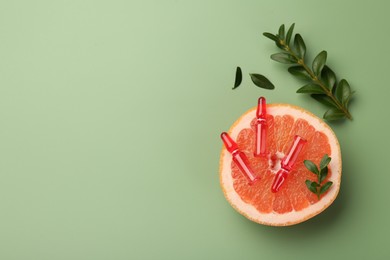 Photo of Skincare ampoules with vitamin C, half of grapefruit and leaves on light green background, flat lay. Space for text