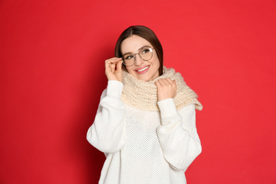 Photo of Young woman wearing warm sweater and scarf on red background. Winter season