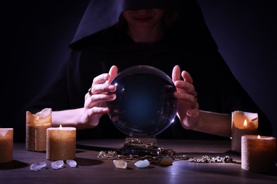 Soothsayer using crystal ball to predict future at table in darkness, closeup. Fortune telling