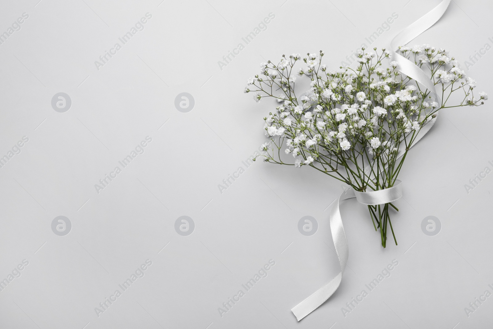 Photo of Beautiful bouquet of white gypsophila flowers with ribbon on light grey background, top view. Space for text