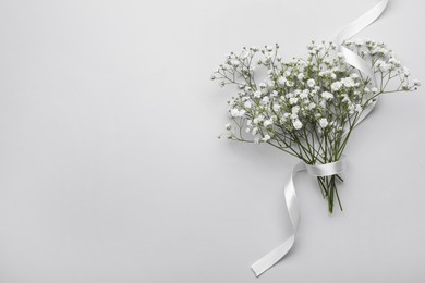 Beautiful bouquet of white gypsophila flowers with ribbon on light grey background, top view. Space for text