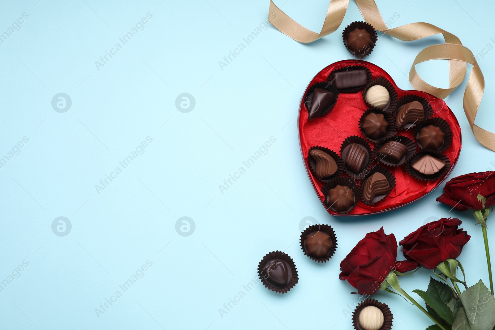 Photo of Heart shaped box with delicious chocolate candies, roses and ribbon on light blue background, flat lay. Space for text