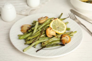Photo of Delicious baked green beans with lemon and mushrooms on white table, closeup