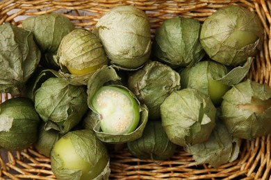 Photo of Fresh green tomatillos with husk in wicker basket, top view