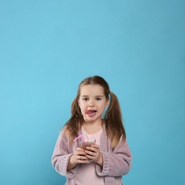 Photo of Cute little child with glass of tasty chocolate milk on light blue background