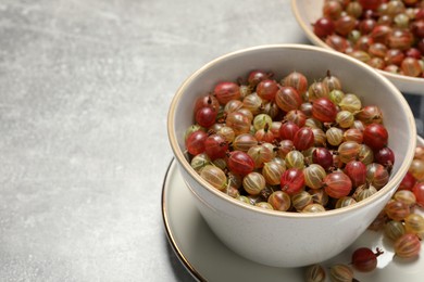 Fresh ripe gooseberries in bowls on light grey table. Space for text
