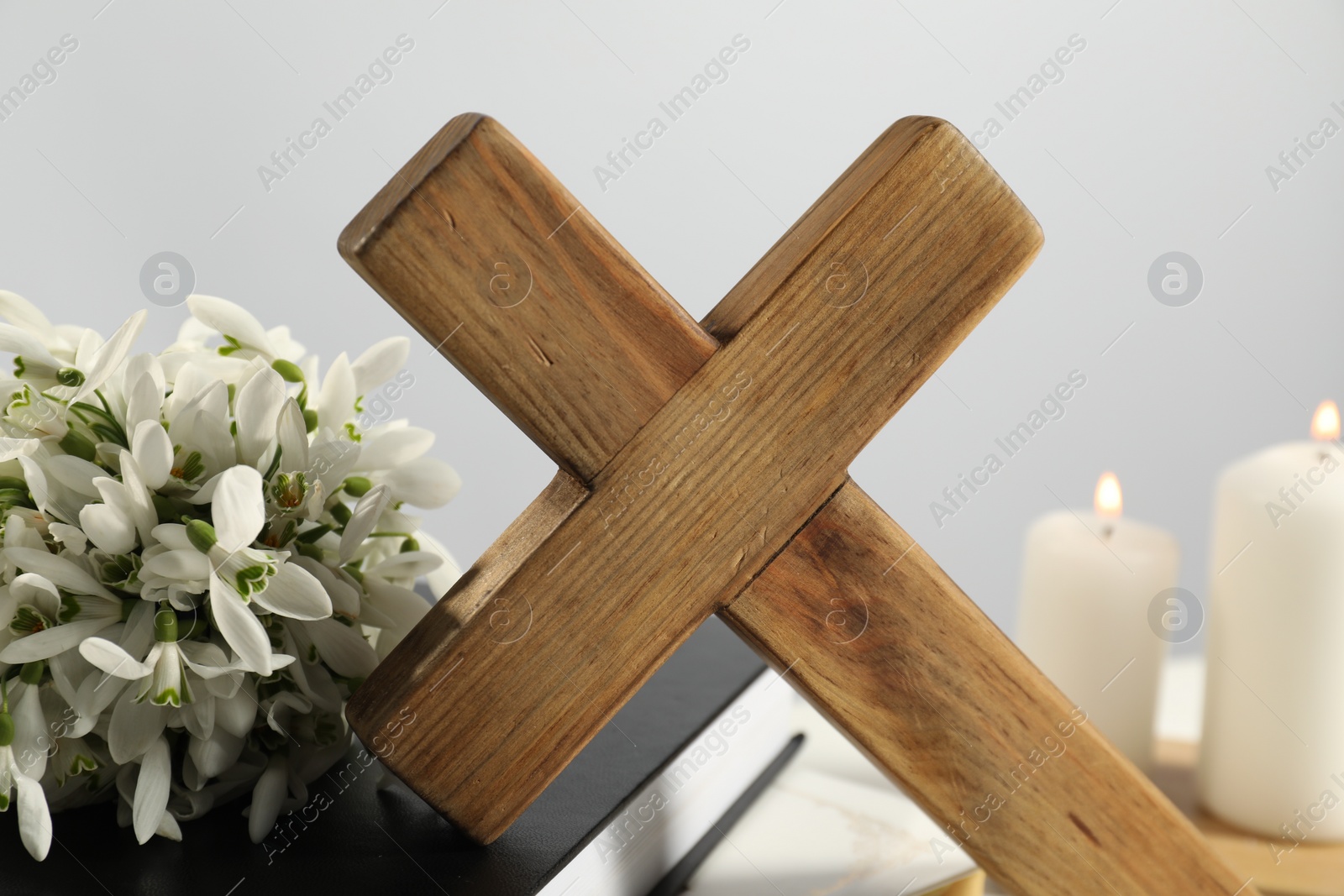 Photo of Wooden cross, Bible, flowers and church candles on table, closeup