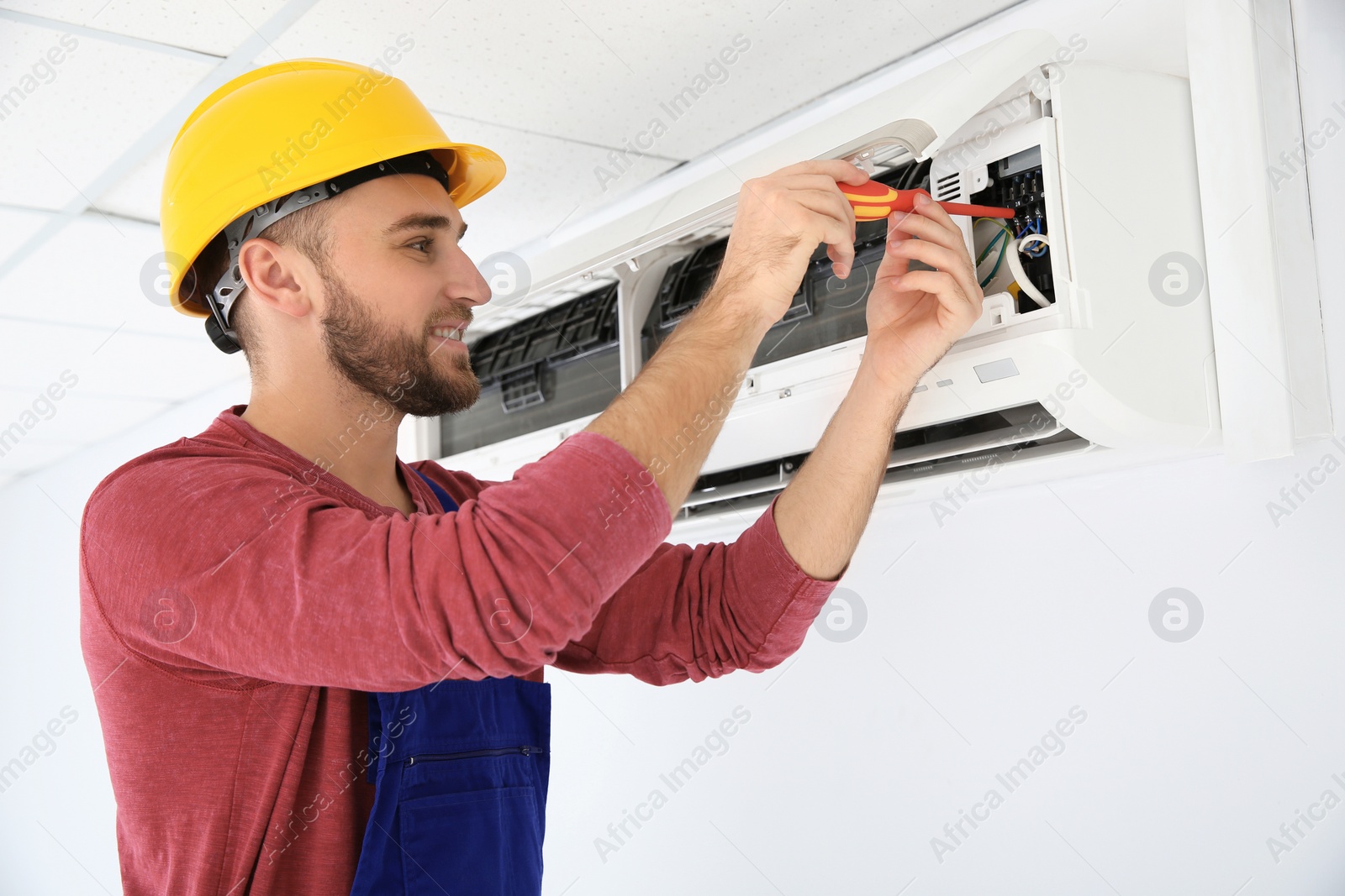 Photo of Electrician with screwdriver repairing air conditioner indoors