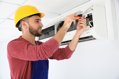 Electrician with screwdriver repairing air conditioner indoors