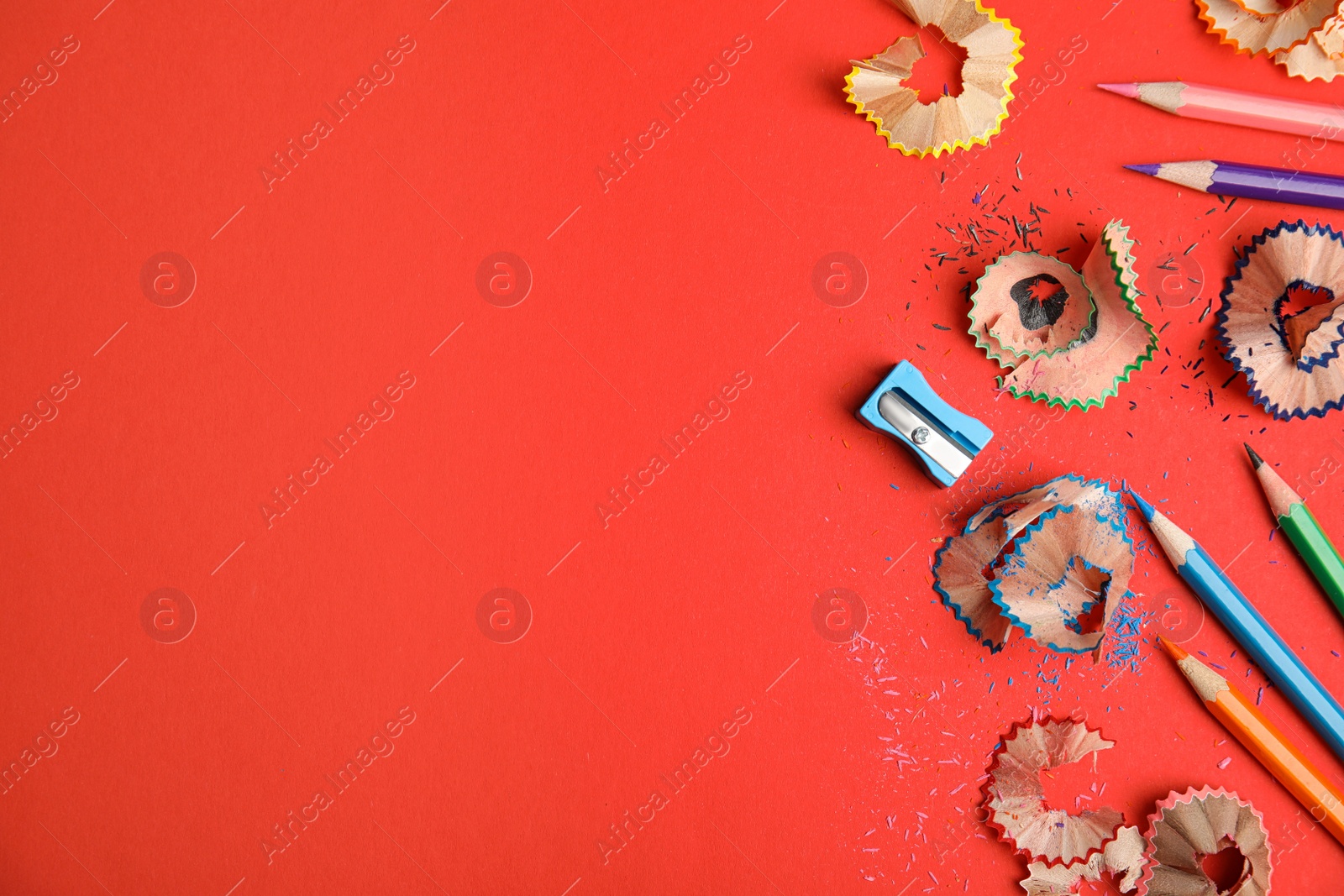 Photo of Color pencils, sharpener and shavings on red background, flat lay. Space for text