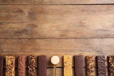 Different tasty bars and scoop of protein powder on wooden table, flat lay. Space for text